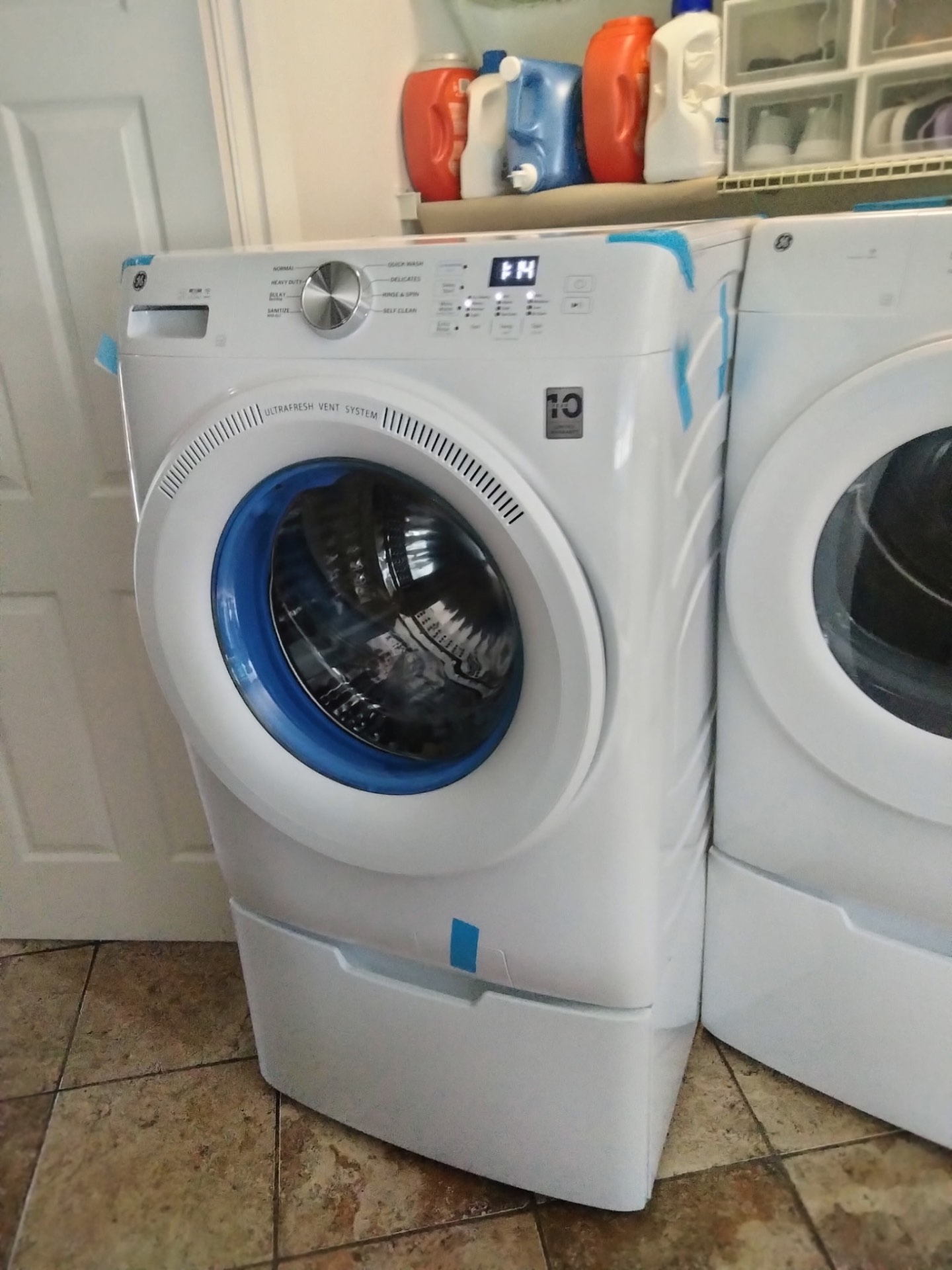 New white GE front-load washer on its pedestal, set in place in a laundry room