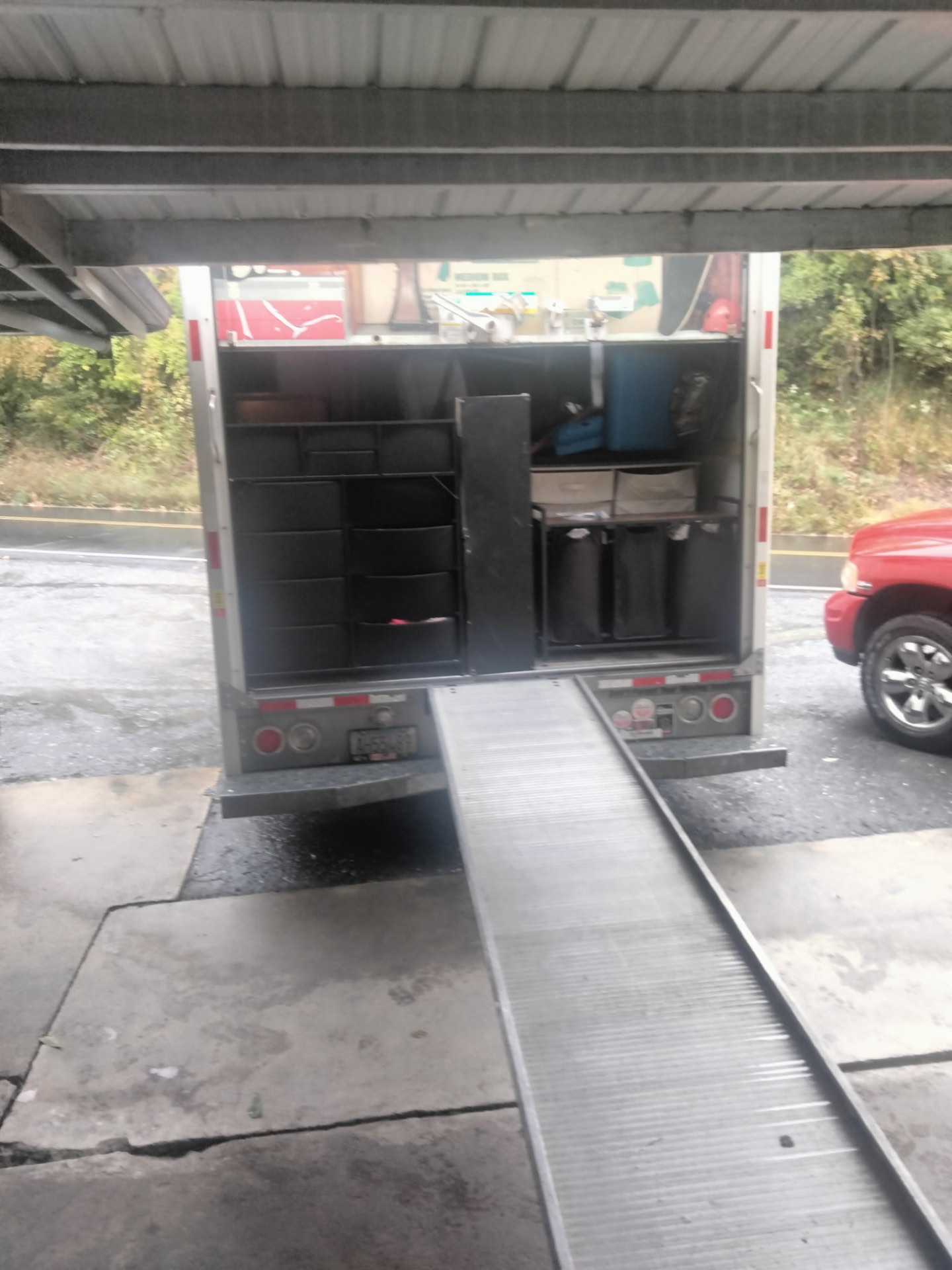 Rear of a moving truck packed with dressers and storage bins, ramp extended to the curb