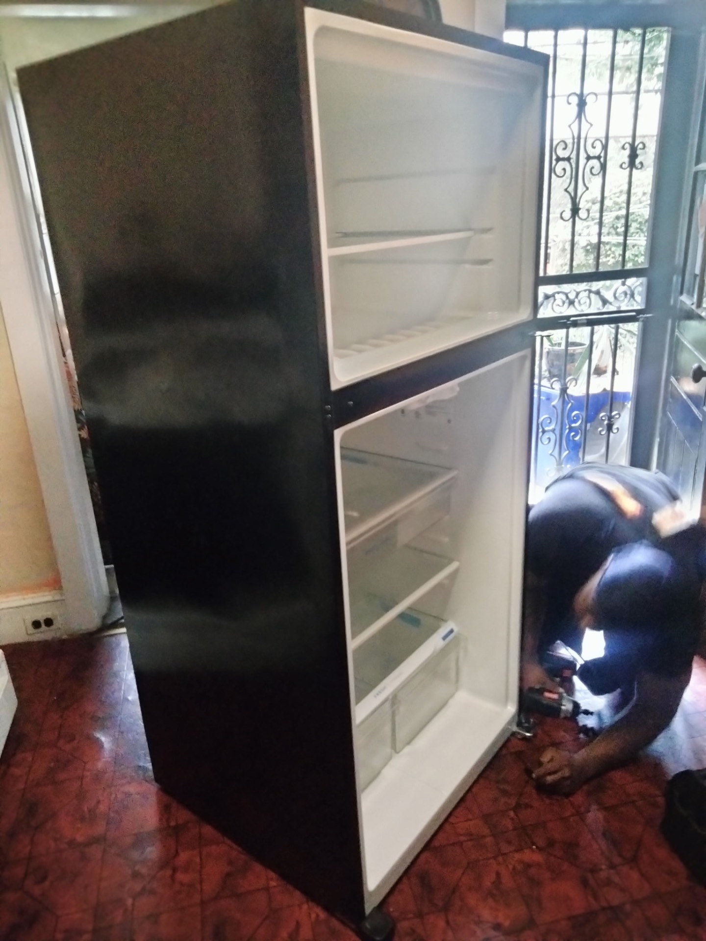 Crew member reattaching the door on a black top-freezer refrigerator in a kitchen