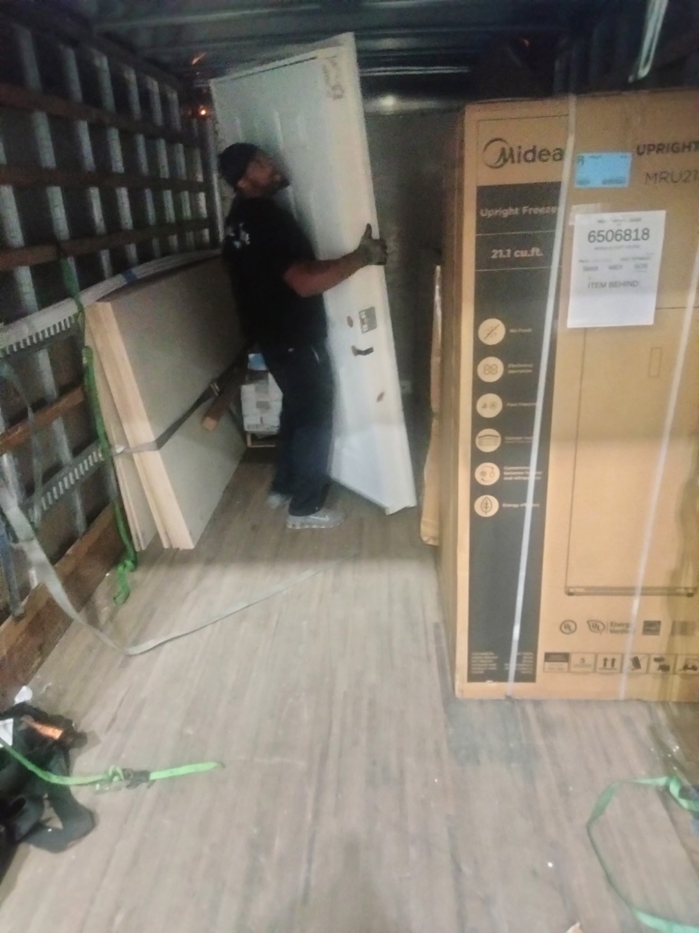 Crew member carrying a large panel inside a box truck beside a boxed upright freezer