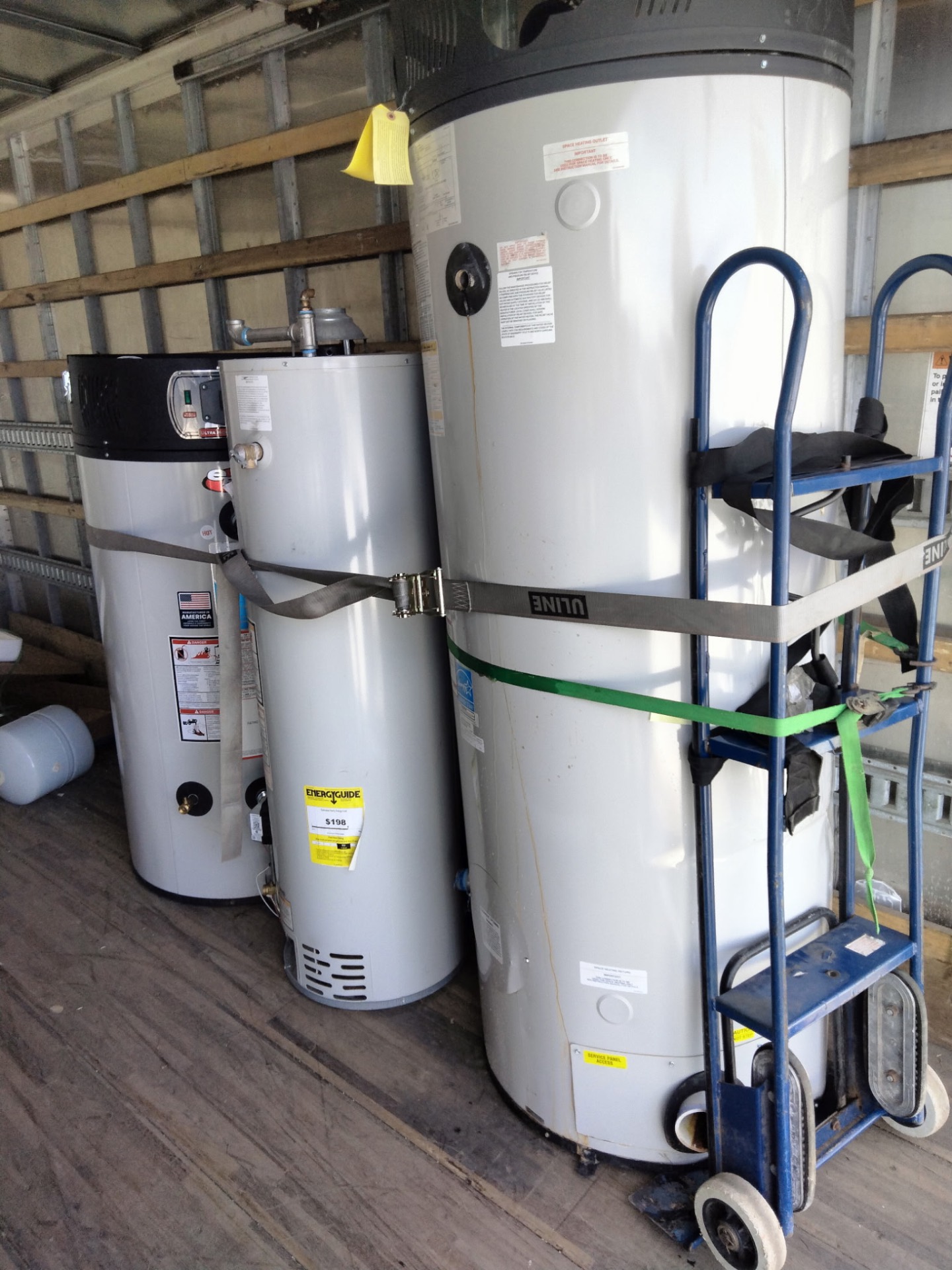 Water heaters secured with straps next to a hand truck inside the moving truck