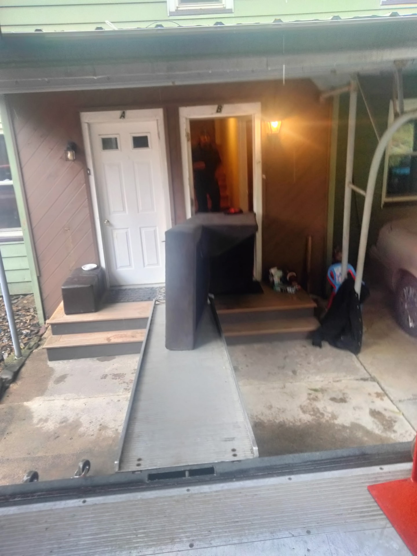 Mover guiding a sectional sofa piece out of a townhouse doorway toward the truck ramp