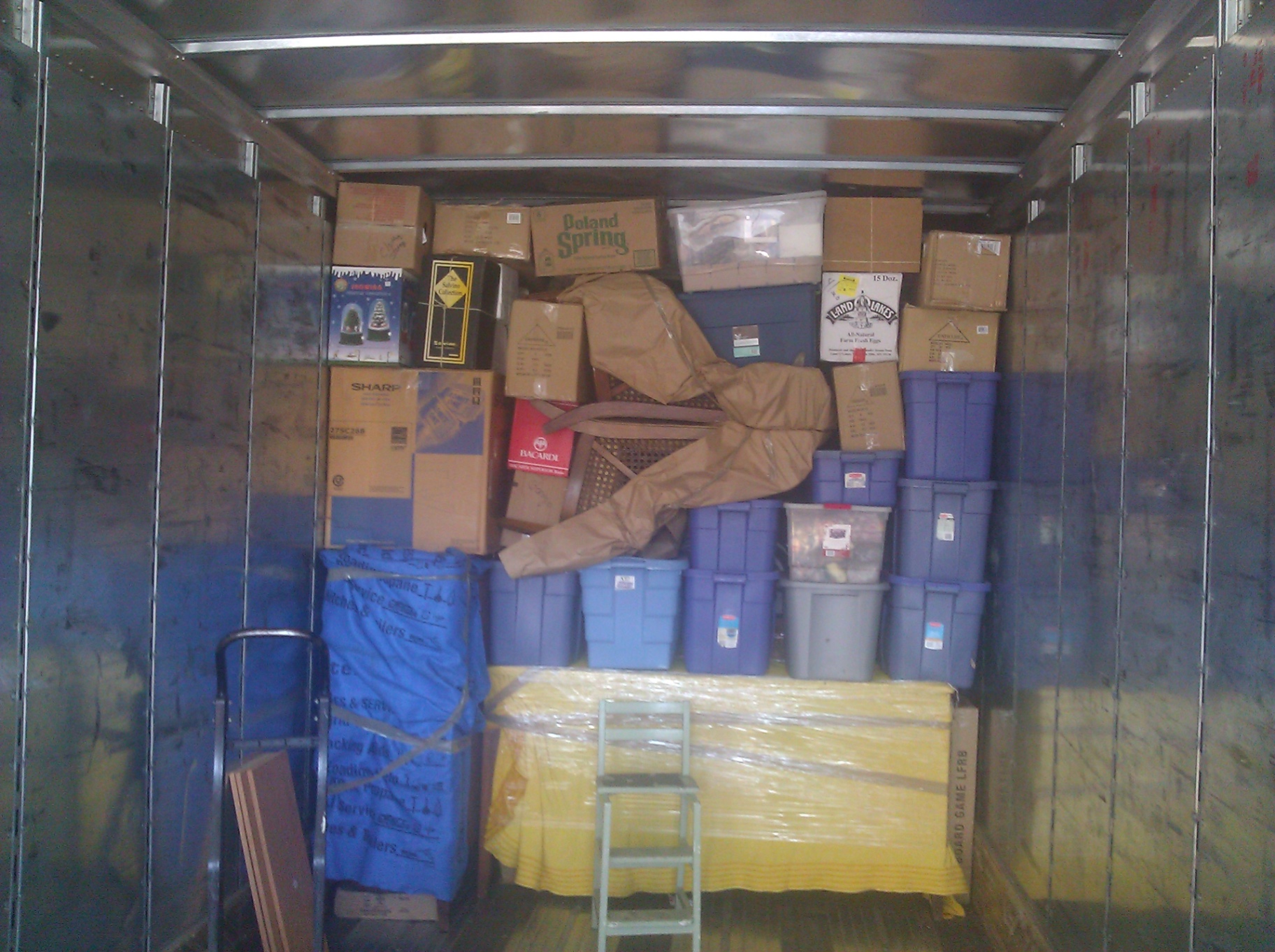 Moving truck packed tightly floor to ceiling with boxes, storage bins, and a plastic-wrapped table and chair
